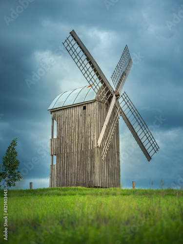 old wooden windmill in green wheat field under deep clouds