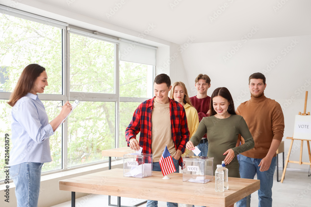 Fototapeta premium Voting young people with USA flag near ballot boxes at polling station