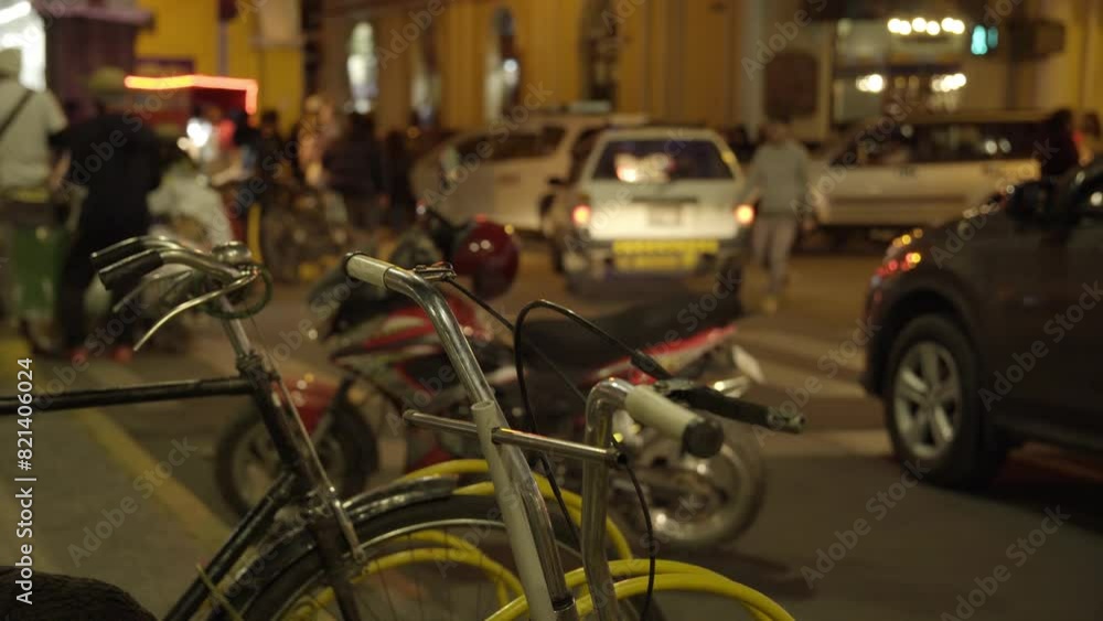 nighttime cityscape of a bicycle parking in a public place, cars and people out of focus in the background, 