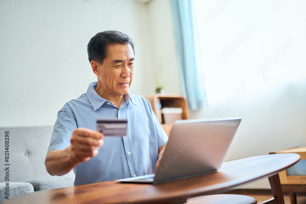 ネットショッピングでクレジットカード番号を打ち込むシニア男性 ネットショッピングでクレジットカード番号を打ち込むシニア男性
