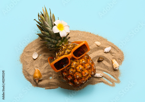 Pineapple in sunglasses, sand and seashells on blue background. Summer concept