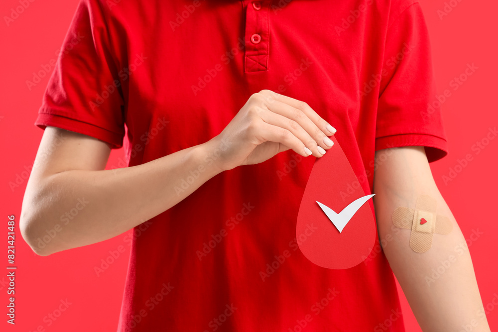 Female blood donor with applied patch and paper drop on red background, closeup Female blood donor with applied patch and paper drop on red background, closeup