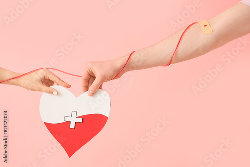 People with paper heart and tube on pink background. Blood donation concept