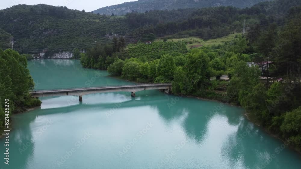 Drone view of turquoise mountain lake and bridge across it. emerald lake lies nestled in rocky terrain and dense forest. bridge spans lake, showcasing tranquil lake, bridge and surrounding nature Drone view of turquoise mountain lake and bridge across it. emerald lake lies nestled in rocky terrain and dense forest. bridge spans lake, showcasing tranquil lake, bridge and surrounding nature