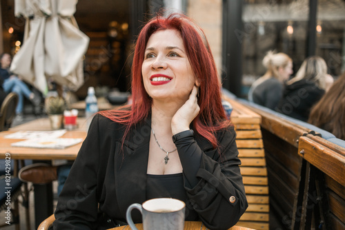 Beautiful happy woman with long red hair enjoying coffee in a street cafe