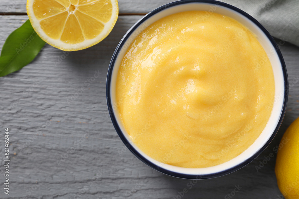 Delicious lemon curd in bowl, fresh citrus fruit and green leaf on grey wooden table, top view. Space for text Delicious lemon curd in bowl, fresh citrus fruit and green leaf on grey wooden table, top view. Space for text