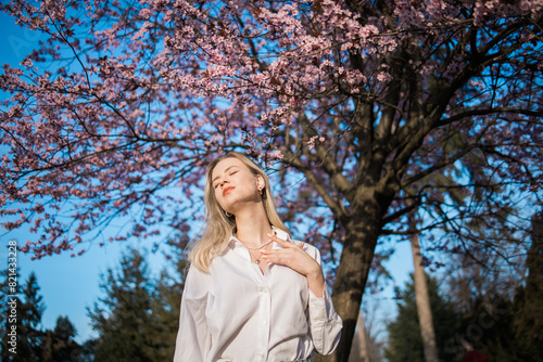 Woman with cherry flowers surrounded by blossoming trees copy space. Beauty and seasonal change and spring bloom season concept.