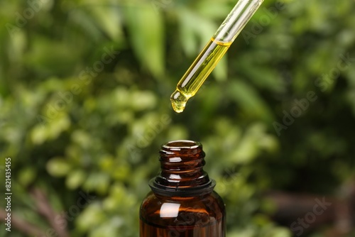 Dripping essential oil from pipette into bottle outdoors, closeup