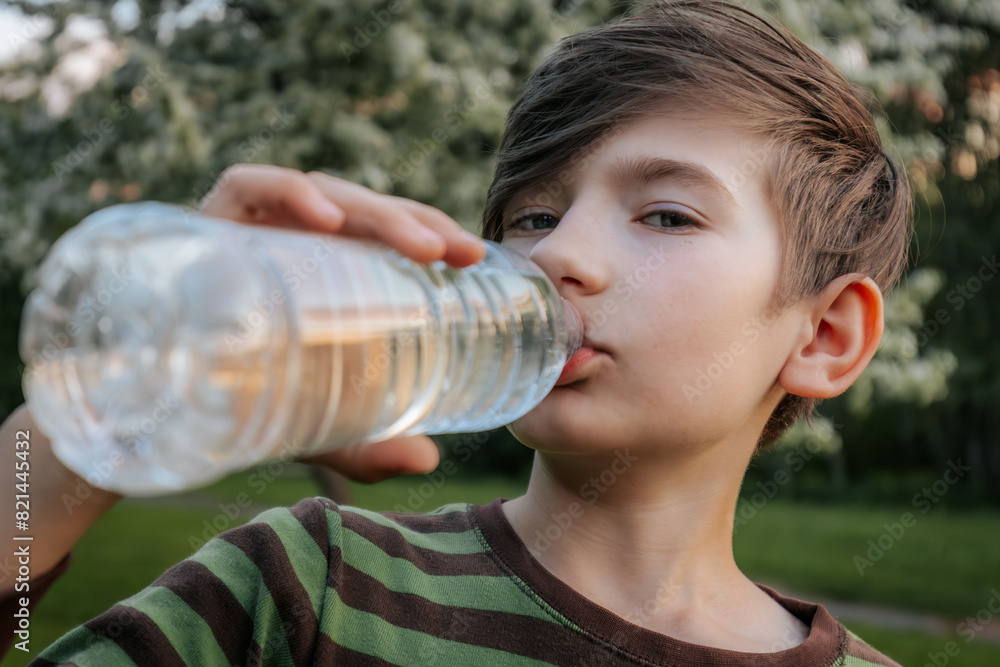young boy drinking water from a plastic bottle, wearing a striped shirt, with a blurred green outdoor background. young boy drinking water from a plastic bottle, wearing a striped shirt, with a blurred green outdoor background.