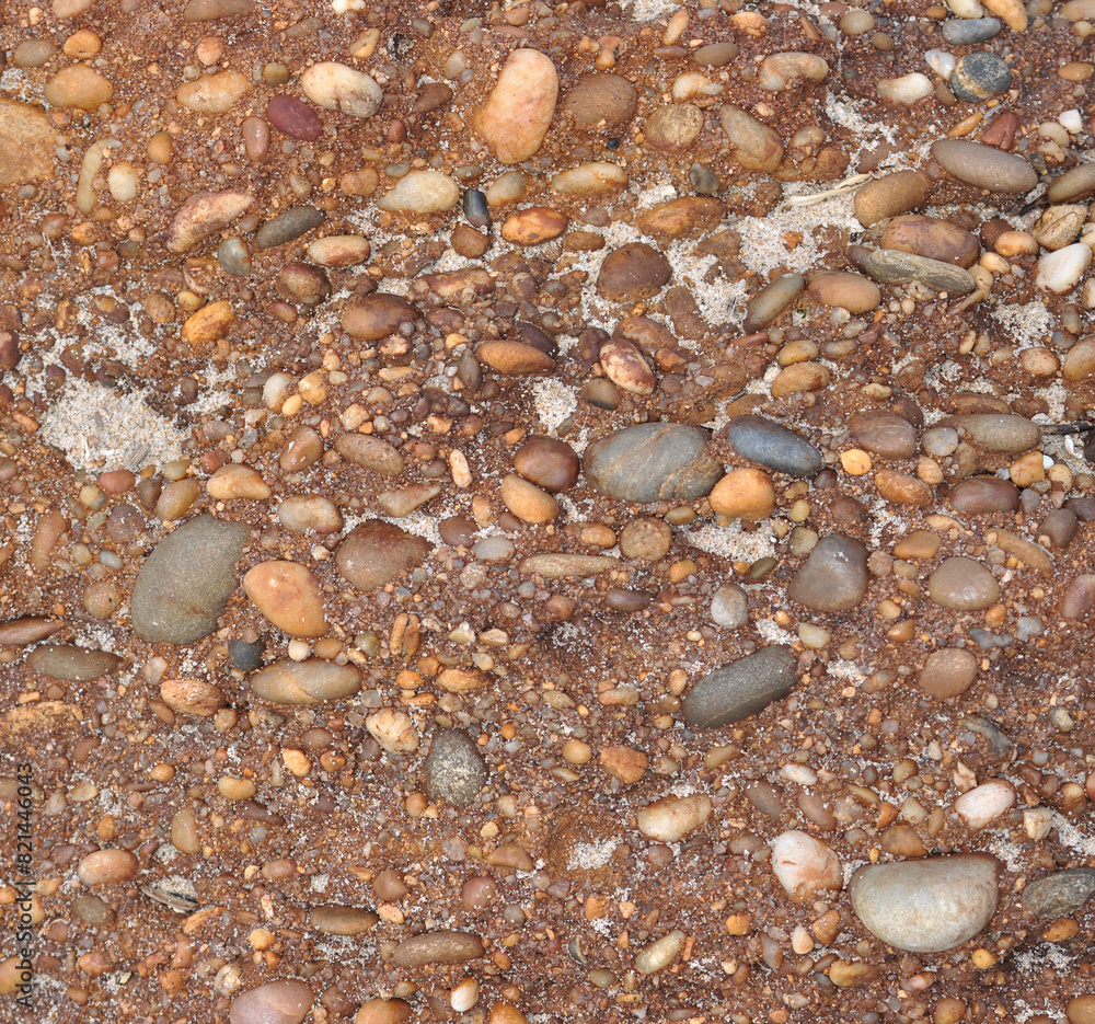 Surface texture of a rock with small sea stones clinging to it by erosion, beach sand spread across the surface of the stone Surface texture of a rock with small sea stones clinging to it by erosion, beach sand spread across the surface of the stone