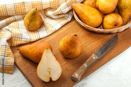 Cutting board with whole and halves pears, wicker basket and yellow kitchen towel on white wooden background..