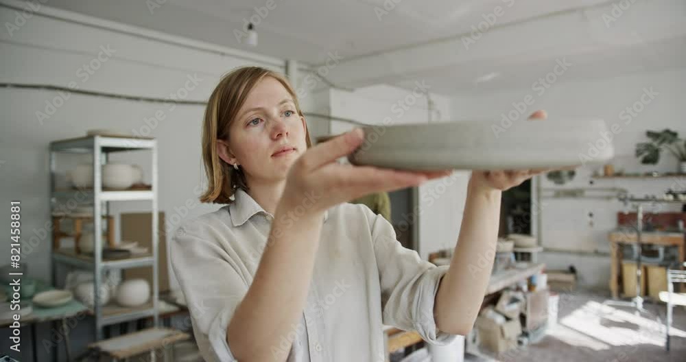 Female Potter Evaluating Ceramic Dish in Spacious Workshop Female Potter Evaluating Ceramic Dish in Spacious Workshop