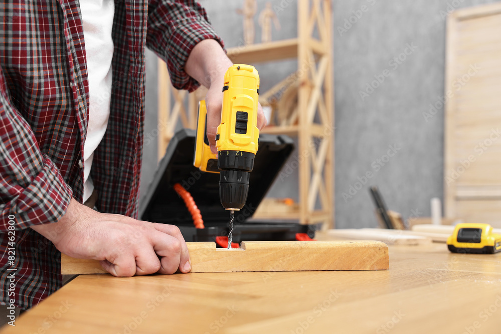 Young handyman working with electric drill at table in workshop, closeup Young handyman working with electric drill at table in workshop, closeup