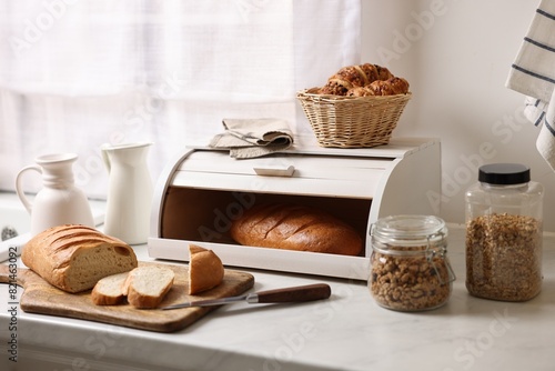 Wooden bread basket with freshly baked loaves on white marble table in kitchen photo