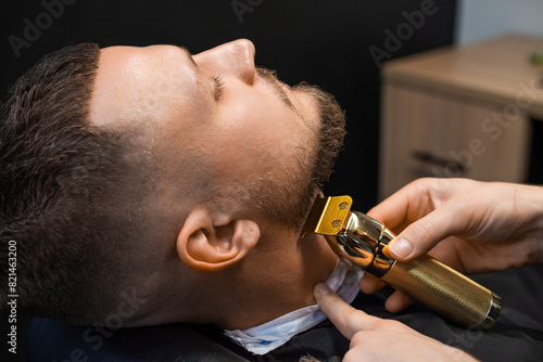 Barber shearing beard to man in barbershop, close up.