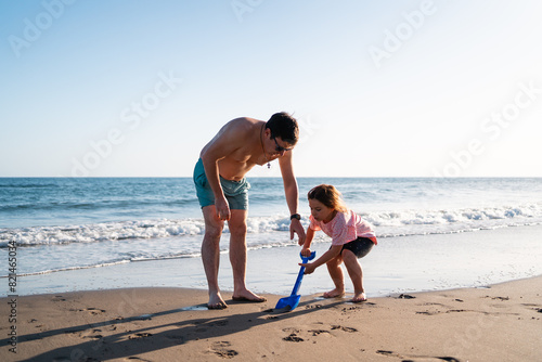 Adult male and young child engage in playful activities with sand toys on a sunny beach, creating lasting memories.