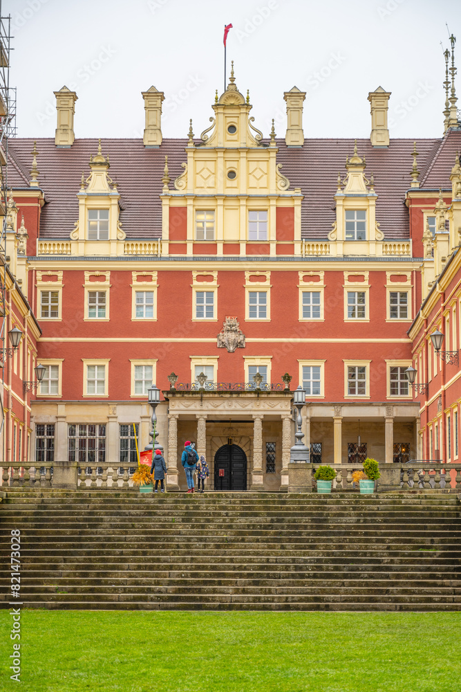 Naklejka premium The front view of Chateau Bad Muskau, with visitors on the entrance steps, under a grey, overcast sky. Saxony, Germany