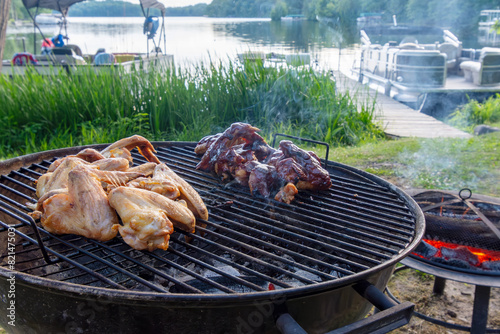 Chicken wings, plain and barbequed, roast on the grill of a northwoods cabin.  Lake and boats in background. photo