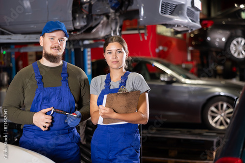Positive car mechanic standing in auto service shop together with female worker ready to take note