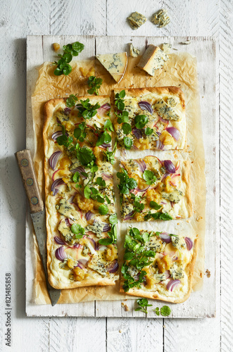 Homemade tarte flambée with blue cheese, pear chutney, red onions and watercress on a white wooden background