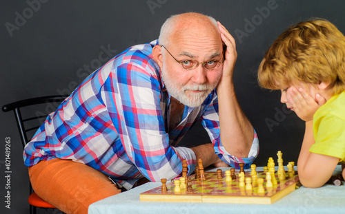 Chess competition. Child boy play chess with grandfather. Board games. Granddad and grandchild playing chess. Brain development and logic concept. Little boy thinking about next move in game of chess.