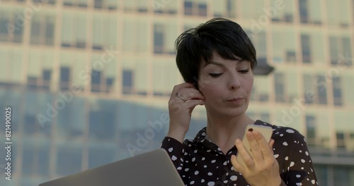 Successful Busy businesswoman multitasking while talking with hands-free headphones. Concept of efficiency, productivity, and modern communication technology. Portrait of woman with smatphone. photo