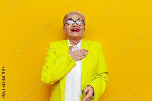 old businesswoman in glasses and business clothes scoff and smiling on a yellow isolated background, elderly pensioner grandmother in blazer laughing and joke photo
