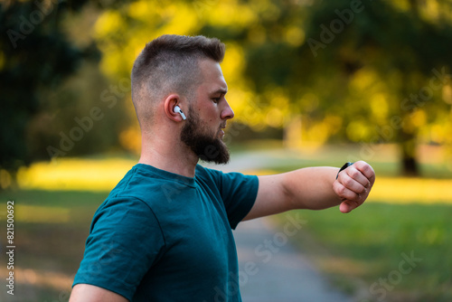 A young runner man looking at a monitor watch checking a heart rate while running or jogging in the park active healthy lifestyle.