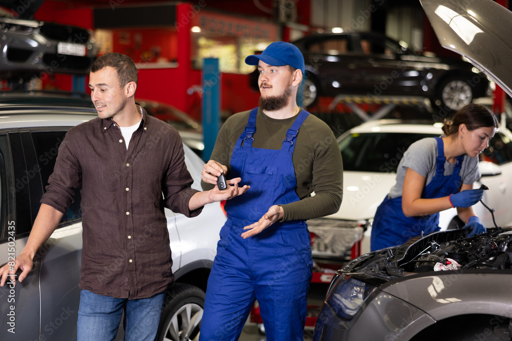 Happy man next to car being repaired. Auto mechanic gives man the keys to his car
