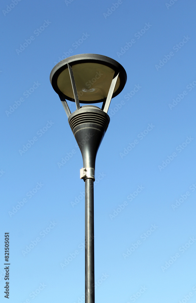 Street lamp light mounted on a slender pole against a clear blue sky Street lamp light mounted on a slender pole against a clear blue sky