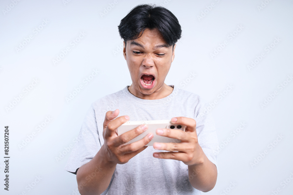Potrait Of Annoyed Young Asian Guy Playing Game On Smartphone And Screaming Isolated On White Background Potrait Of Annoyed Young Asian Guy Playing Game On Smartphone And Screaming Isolated On White Background