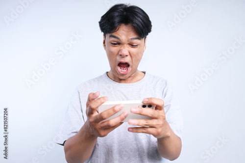 Potrait Of Annoyed Young Asian Guy Playing Game On Smartphone And Screaming Isolated On White Background