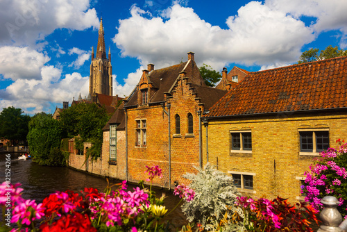 Peaceful photo of canal of Bruges with view of belfry under deep blue cloudy sky.