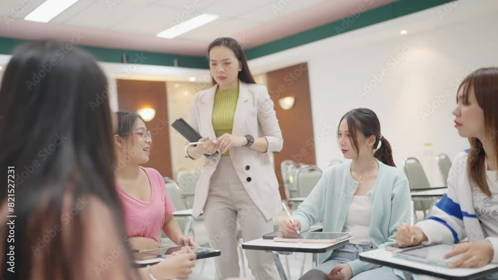 A group of women are sitting in a classroom with a woman standing in front of them. The woman in front of them is holding a clipboard and a black pen. Scene is serious and focused A group of women are sitting in a classroom with a woman standing in front of them. The woman in front of them is holding a clipboard and a black pen. Scene is serious and focused