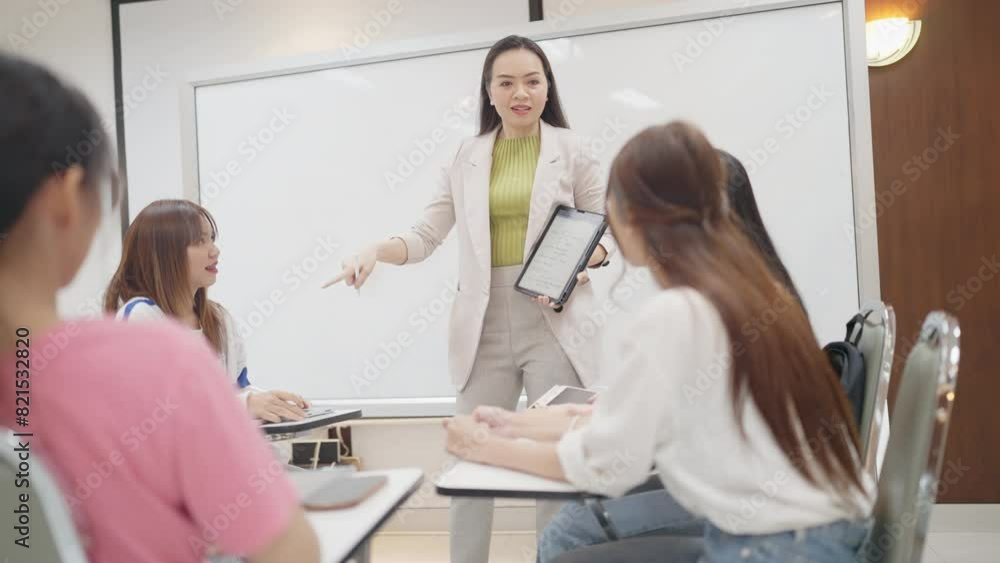 A woman is teaching a group of students. The students are sitting in a classroom and are looking at a tablet A woman is teaching a group of students. The students are sitting in a classroom and are looking at a tablet