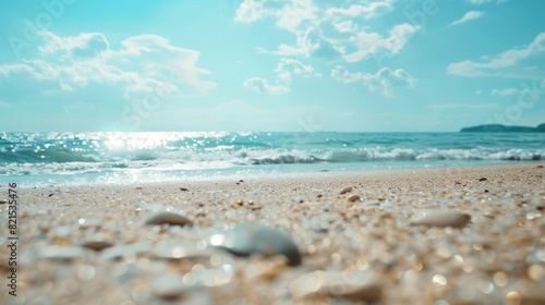 A tranquil beach scene with sun glinting off the sea, clear blue sky and waves gently breaking on the sandy shore