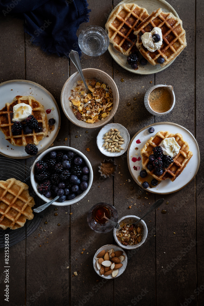 Top view of breakfast granola bowl, belgian waffles with berries and cream on wooden table. Top view of breakfast granola bowl, belgian waffles with berries and cream on wooden table.