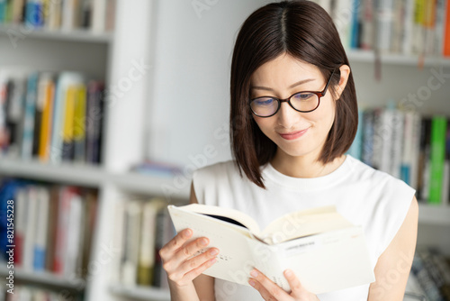 本棚の前でメガネをかけて本を読んでいる女性 photo