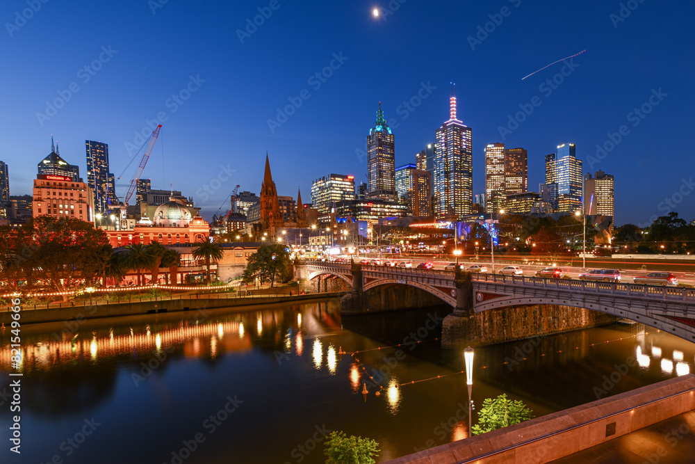 Obraz premium Flinders Street Station and the Melbourne City skyline behind the Yarra River during sunset in Melbourne