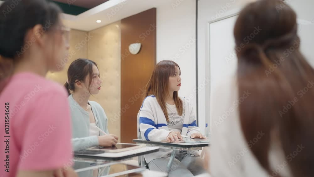 A group of women are sitting at desks in a classroom. One of the women is wearing a blue and white striped shirt A group of women are sitting at desks in a classroom. One of the women is wearing a blue and white striped shirt