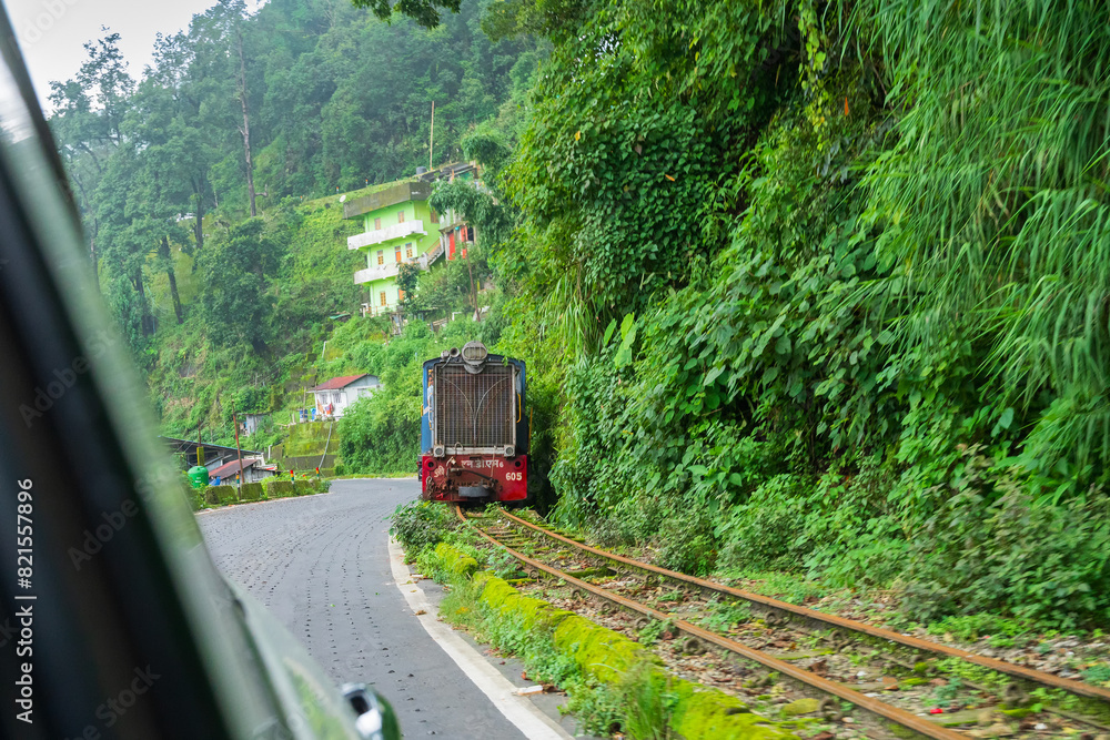 Naklejka premium Darjeeling,West Bengal,India - 10th August 2023 : Diesel Toy train, running over narrow gauge railway between New Jalpaiguri and Darjeeling, beside Himalayan roads. Darjeeling Himalayan Railway,
