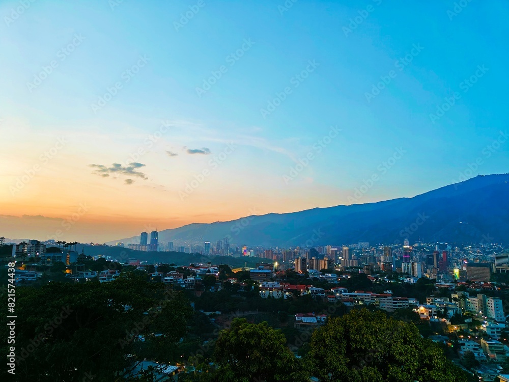 Fototapeta premium Atardecer con vista a la ciudad de Caracas en Venezuela. Cielo azul, poca nubosidad y horizonte color naranja.