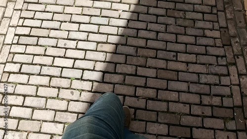 man walking on cobblestone street wearing blue jeans and gray brown sneakers (pov point of view looking down at ground taking steps) brick walkway in san juan puerto rico sun and shade photo