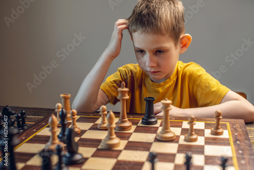 The child is a boy playing chess alone at the board. The process of thinking about a move to checkmate