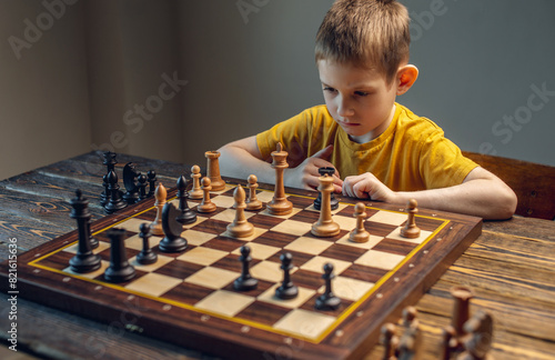 The child is a boy playing chess alone at the board. The process of thinking about a move to checkmate