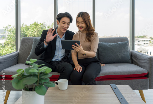 A man and woman waving hand via remote communication through tablet computer monitor  while sit on sofa in the living room.