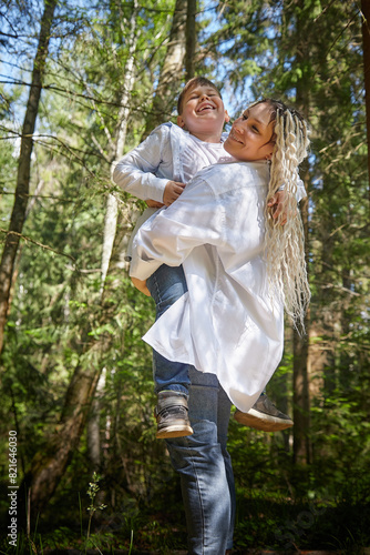 Funny mother with dreadlocks and fat boy happy walking in the woods on a sunny summer day