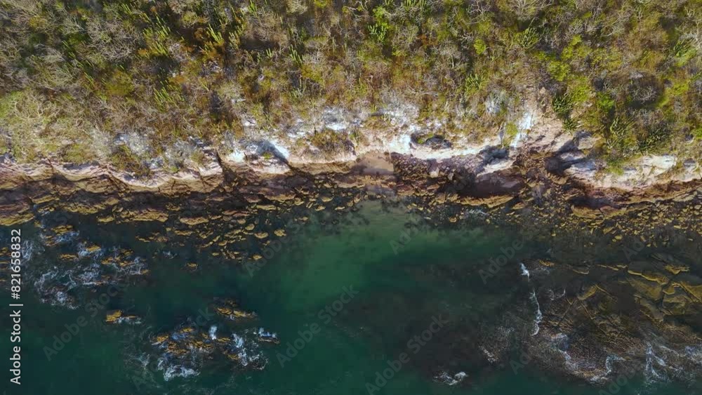 Aerial video of a deserted island with contrasting rocky and sandy shores, lush green trees, birds soaring above, and gentle waves caressing the coastline, creating a serene natural landscape. Aerial video of a deserted island with contrasting rocky and sandy shores, lush green trees, birds soaring above, and gentle waves caressing the coastline, creating a serene natural landscape.