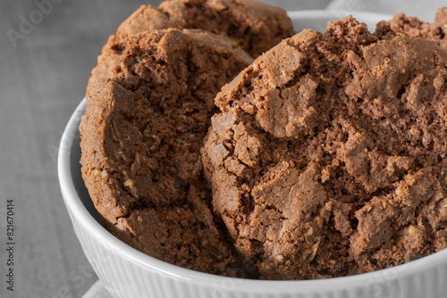 Chocolate flavoured cookies, with chocolate chips, in a bowl on a tablecloth with a wooden background.