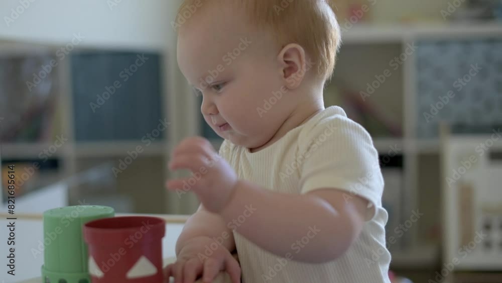 A curious toddler engages with green and red Montessori cups in a playroom, enhancing fine motor skills and color recognition in a stimulating educational environment A curious toddler engages with green and red Montessori cups in a playroom, enhancing fine motor skills and color recognition in a stimulating educational environment